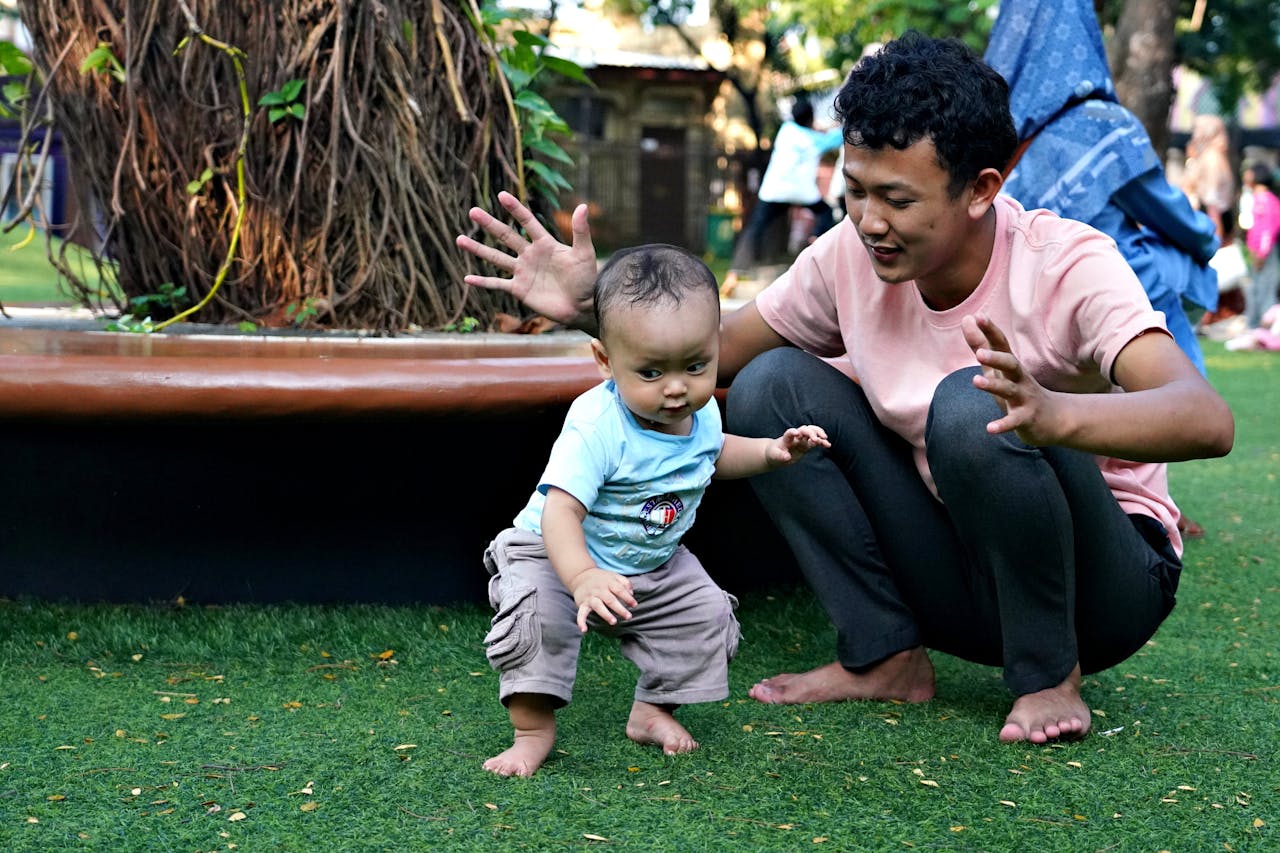 father-supports-toddler-s-first-steps-outdoors-34247130